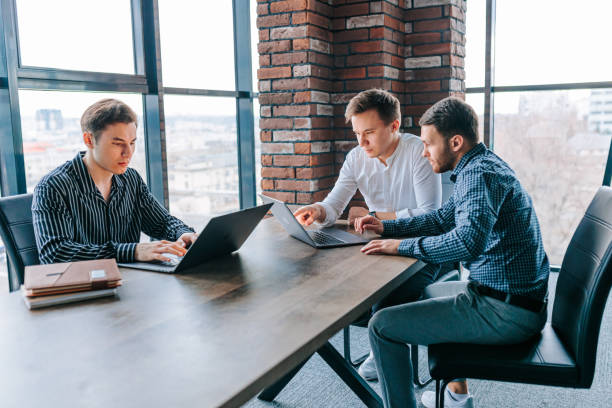 istock Three young men collaborating with their mentor over a laptop in a corporate office. 2155530591