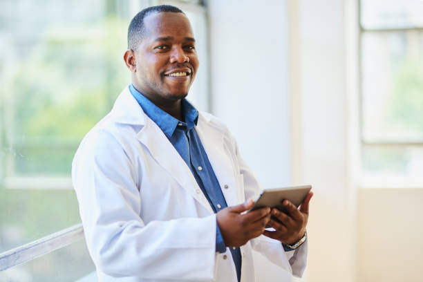 istock Confident Black Doctor Smiling, Holding Tablet in Modern Hospital Setting 2155531155