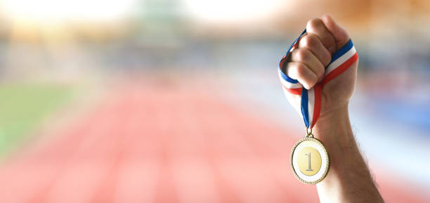 istock Hand showing gold medal and athletics stadium behind 2155532762