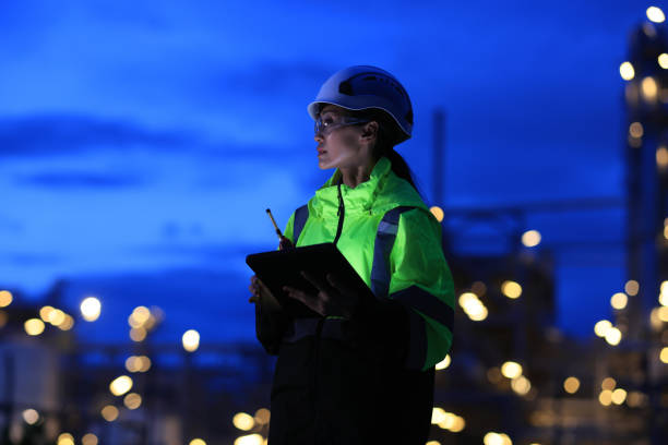 istock Female Industrial Engineer wearing safety vest and hardhat using digital tablet working at nightshift 2155546001