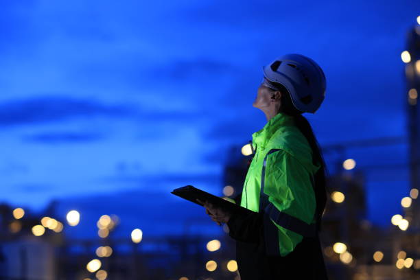 istock Female Industrial Engineer wearing safety vest and hardhat using digital tablet working at nightshift 2155546002