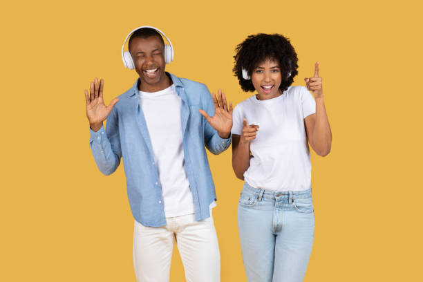 Couple with headphones and dancing gestures on yellow