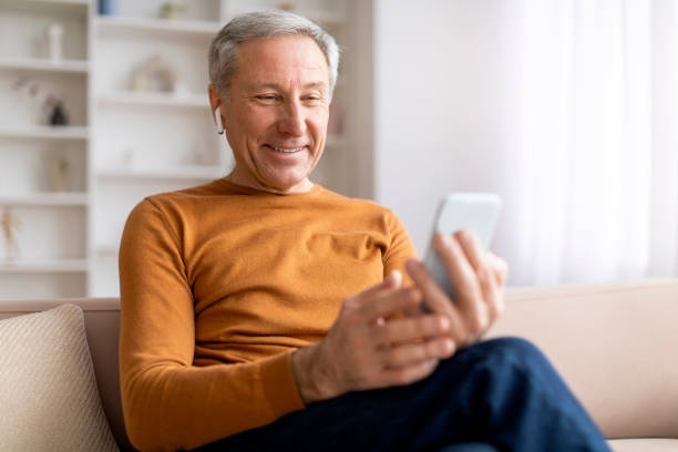istock Happy senior man sitting on couch, using phone and earphones 2155547431