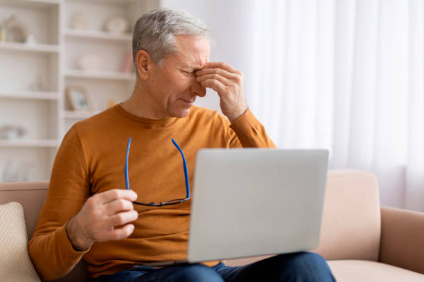 istock Senior man rubbing eyes while using laptop at home 2155547442