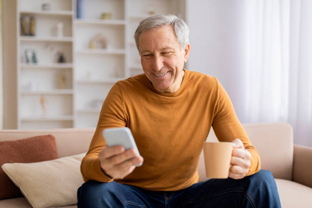 istock Cheerful senior holding mug and smartphone 2155547450
