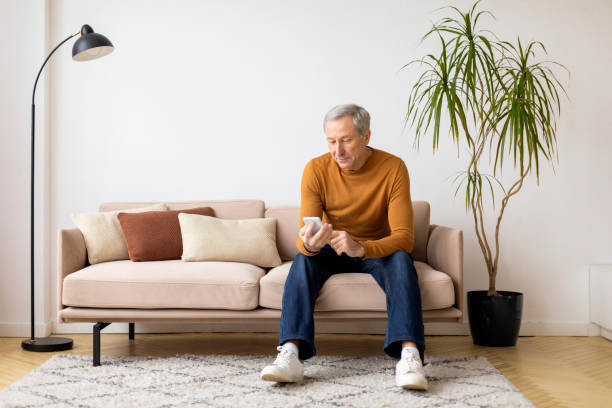 istock Senior man sitting on couch using smartphone 2155547468