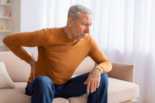 istock Unhappy grandfather sitting on couch and rubbing his lower back 2155547581
