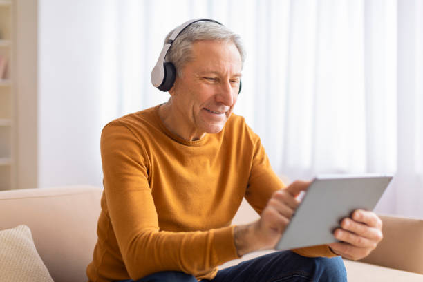 istock Elderly man concentrating on tablet with headphones 2155547605