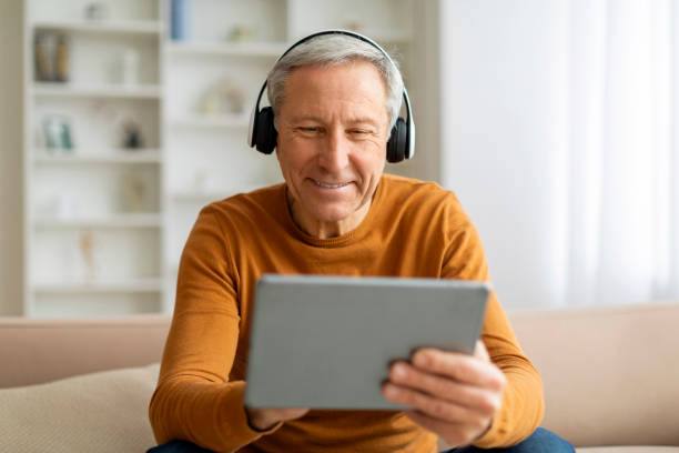 istock Positive elderly man using digital tablet and headphones at home 2155547645