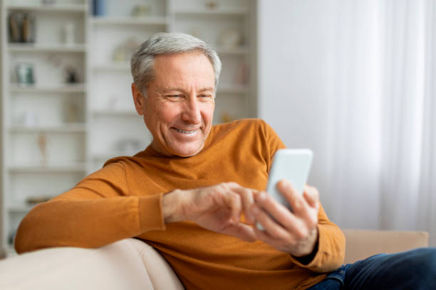istock Happy elderly man resting on couch at home, using smartphone 2155547652