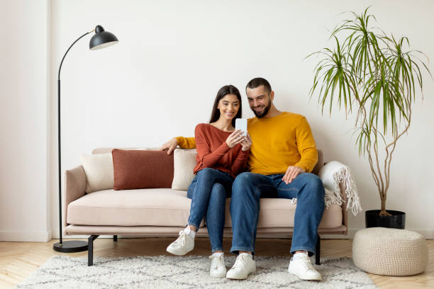 istock Young Smiling Caucasian Couple Using Mobile Phone And Embracing Together At Home 2155547928