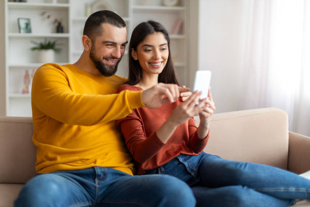 istock Happy young man and woman using smartphone while relaxing on couch together 2155547935