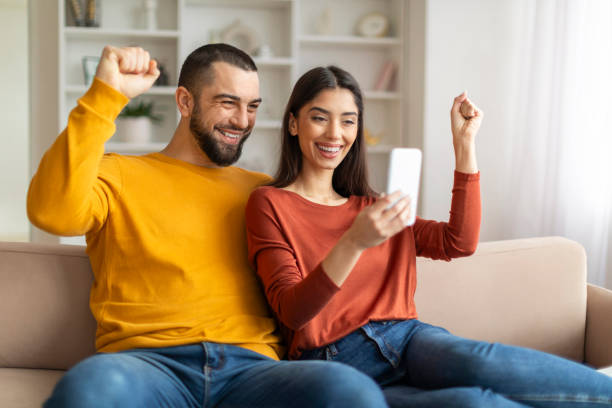 istock Happy Young Couple Celebrating Success While Looking At Smartphone Screen At Home 2155547973
