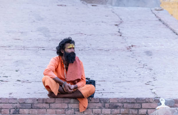 Varanasi, Uttar Pradesh, India - March 2023: Portrait of old holy sadhu baba in traditional dress sitting on the ghats near ganges in varanasi.