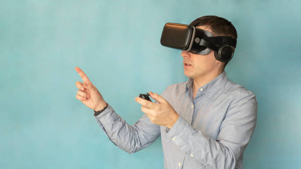 istock Modern technologies and domestic entertainment concept. Young man trying virtual reality , using headset VR glasses and holding joystick, playing video games on a blue background. , copy space 2155551879