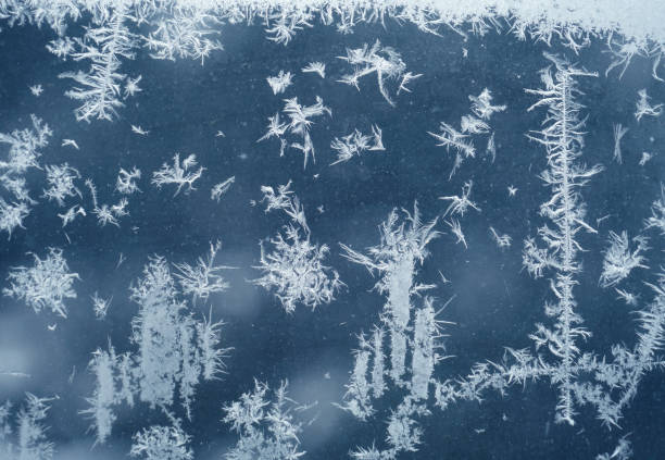 Intricate ice crystals form on a frosted window, creating a beautiful winter scene