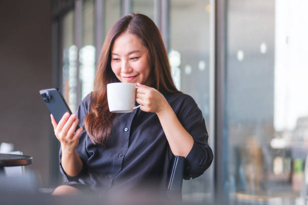 istock Portrait image of a young woman holding and using mobile phone while drinking coffee in cafe 2155555776