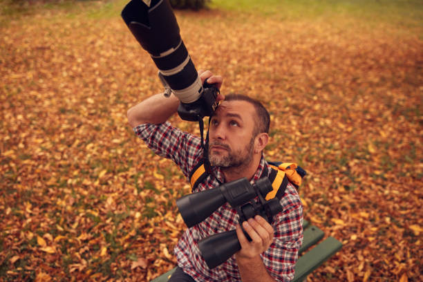 Man using binoculars and camera for bird and animal watching in nature.
