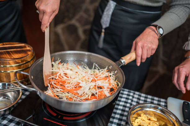 Multiracial group experience and learn the art of Chinese cuisine as they skillfully prepare ingredients for a flavorful vegetable stir-fry delight on a cooking class with beautiful Chinese female chefs.
