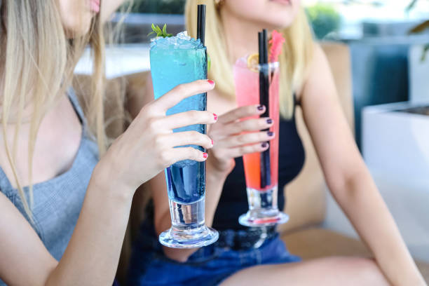 istock Two Women Sitting on a Couch Holding Drinks 2155564168