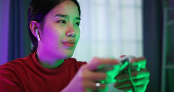 istock Young woman wearing wireless headphones and joystick controller is excited while having fun playing video games in the living room at home 2155564891