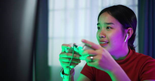 istock Young woman wearing wireless headphones and joystick controller is excited while having fun playing video games in the living room at home 2155564893