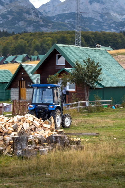 Farm rural landscape with village houses, pile of firewood and tractor, summer or autumn