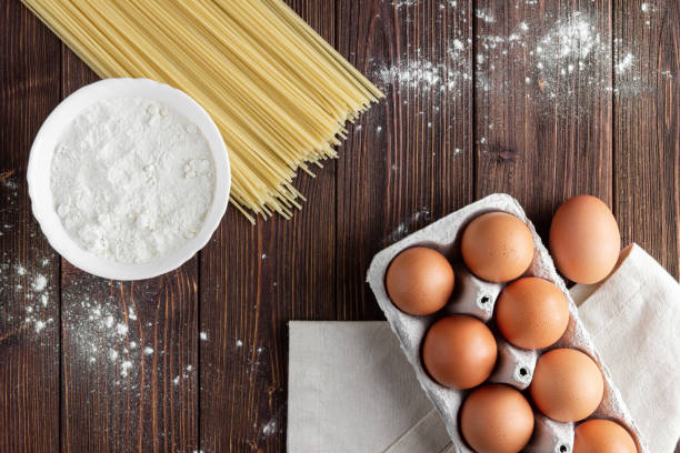 Raw pasta spaghetti with eggs and flour on wooden table. Top view of Italian cuisine ingredient.