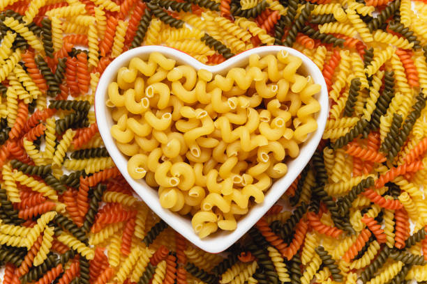 Raw pasta cavatappi in heart bowl on torti texture. Top view of Italian cuisine ingredient.