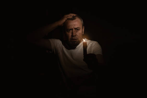 istock Frightened man with a candle during blackout. Man looking at the camera with a candle in the dark 2155576774