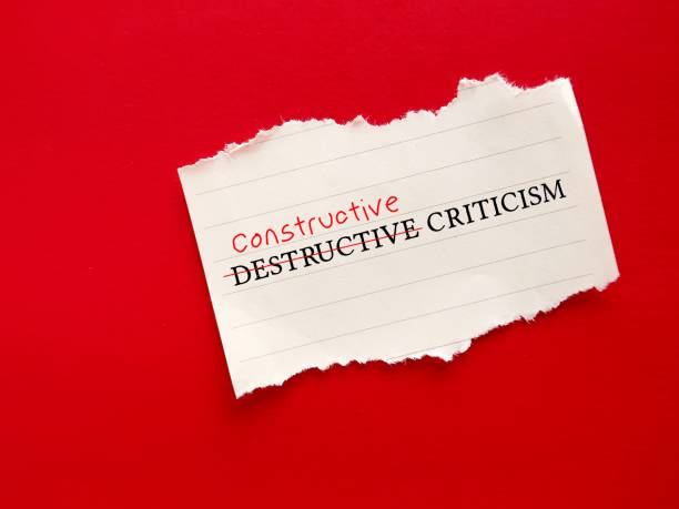 Torn paper on red background with handwritten text DESTRUCTIVE CRITICISM, changed to CONSTRUCTIVE CRITICISM - to shift negative judgement which destroy someone's reputation or self-esteem to actionable advice to help employees to improve papel rasgado sobre fondo rojo con texto escrito a mano crÍtica destructiva, cambiado a crÍtica constructiva: para cambiar el juicio negativo que destruye la reputación o la autoestima de alguien a un consejo práctico para ayudar a los empleados a mejo