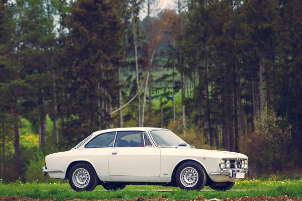 London, UK - May 29, 2025: Like a scene straight out of the sixties, a dark blue 1975 Alfa Romeo Giulia sits at the side of the road in Holland Park, London. Behind it sits another dark blue classic, a 1967 Volvo 1800S. The Volvo was made famous when a white version was used by Roger Moore in the iconic sixties tv show The Saint. Whilst it's getting quite old, this svelt Swedish sports coupe is still a head-turner to this day.