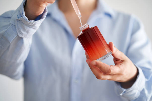 Female hands in a blue shirt hold a pink bottle of serum.