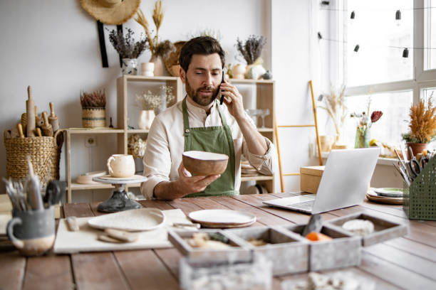 istock Young bearded man potter taking order for purchase of tableware. 2155589078