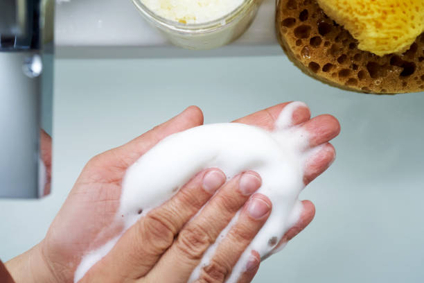 Foam cleanser in female hands over the sink.