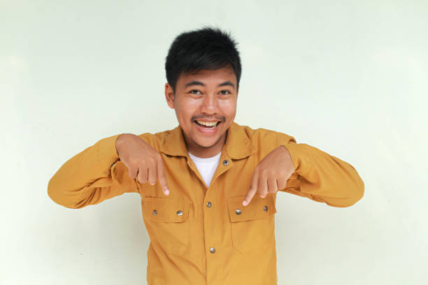 Excited and happy Asian man pointing at the copy space below him, isolated by gray background.