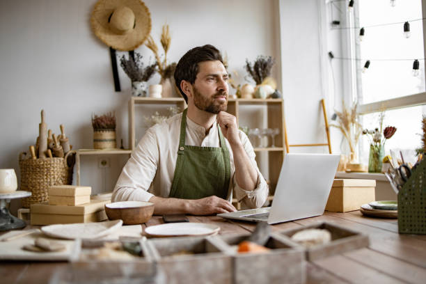istock Relaxing man in apron enjoys break while sitting at table in pottery shop. 2155605400