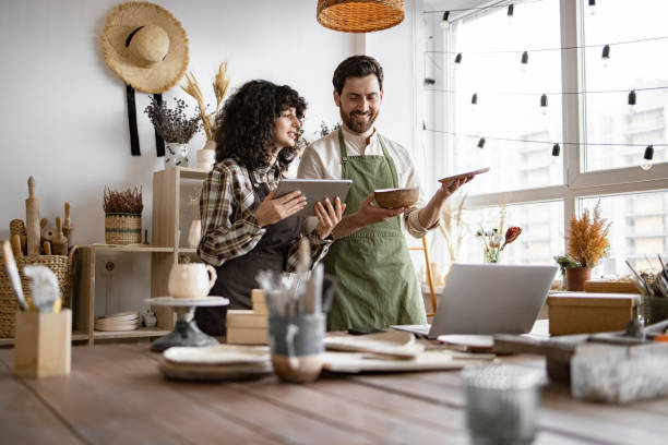 istock Saleswoman typing on digital tablet while bearded seller holding ceramic bowl. 2155605432
