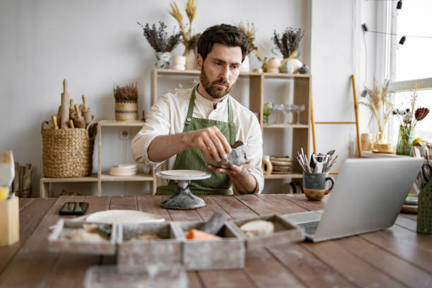 istock Male artisan sculpting clay in a ceramics workshop with laptop 2155605477