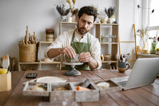 istock Male artisan sculpting clay in a ceramics workshop with laptop 2155605482