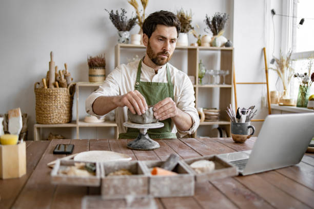 istock Male artisan sculpting clay in a ceramics workshop with laptop 2155605483