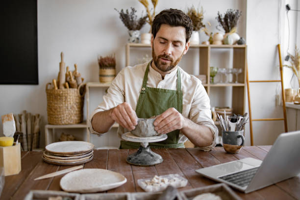 istock Male artist shaping clay pot in rustic studio filled with pottery tools 2155607503