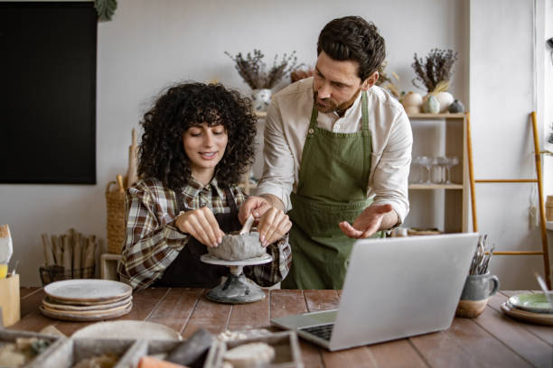 istock Man teaching woman pottery in ceramics workshop with laptop 2155607583