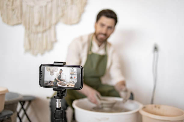 istock Potter making clay vase while recording video blog 2155610083