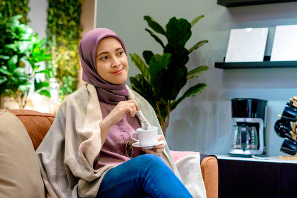 Asian hijab woman enjoying coffee on sofa in modern house