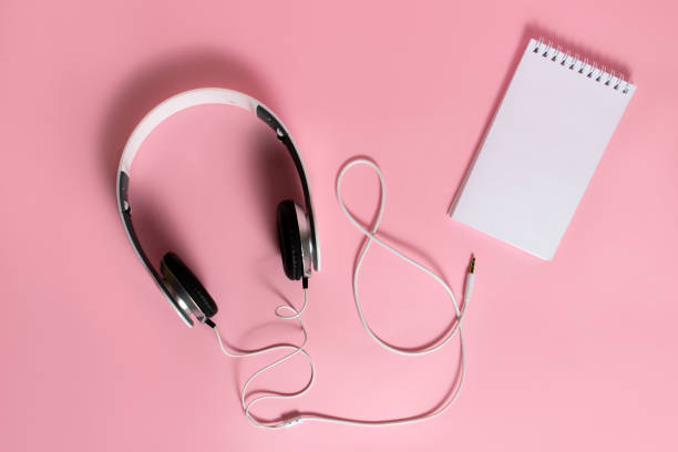 Headphones and blank notepad on pink background. Top view, flat lay background