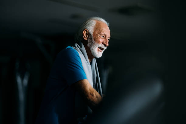 Happy senior man smiling and laughing while taking a break during a workout session at the gym.