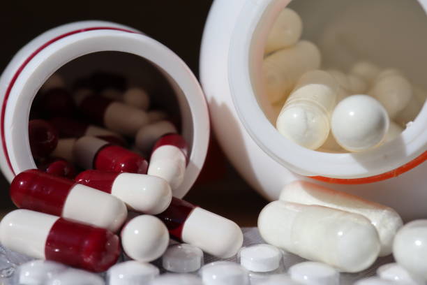 istock White and red capsules pill spilled out from white plastic bottle container. 2155617936
