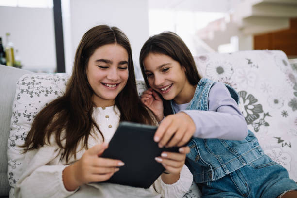 istock Two teenagers sisters sitting on the couch and using digital tablet 2155638669