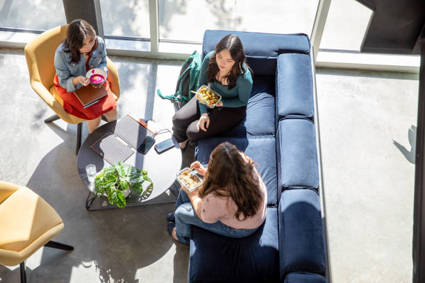 istock Overhead view of diverse group of office workers charging smart phone with portable solar panel while eating a healthy lunch in break room together 2155642990